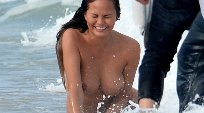 Chrissy Teigen nude in the ocean with wave splashing in her face