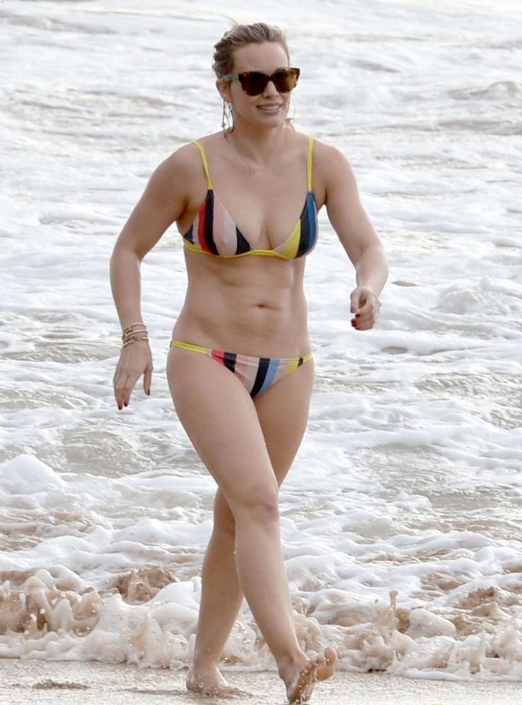 Hilary Duff in a colorful striped bikini with sunglasses on walking on the beach
