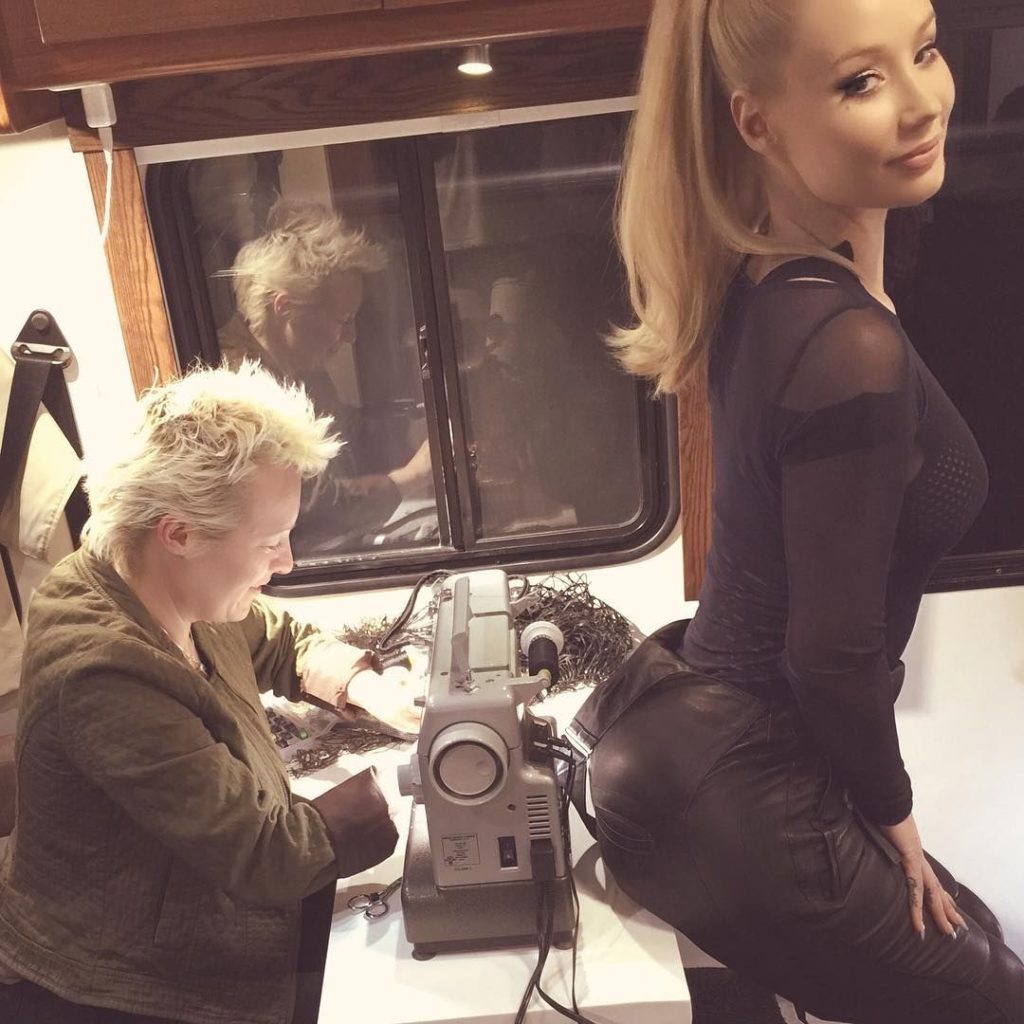 Iggy Azalea sitting by a sewing machine in tight black clothes